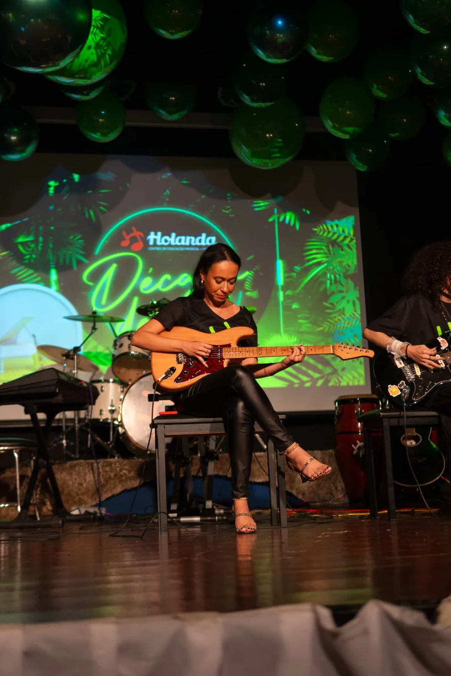 Aluna adulta tocando guitarra no palco em recital da Escola de Música Holanda Premium