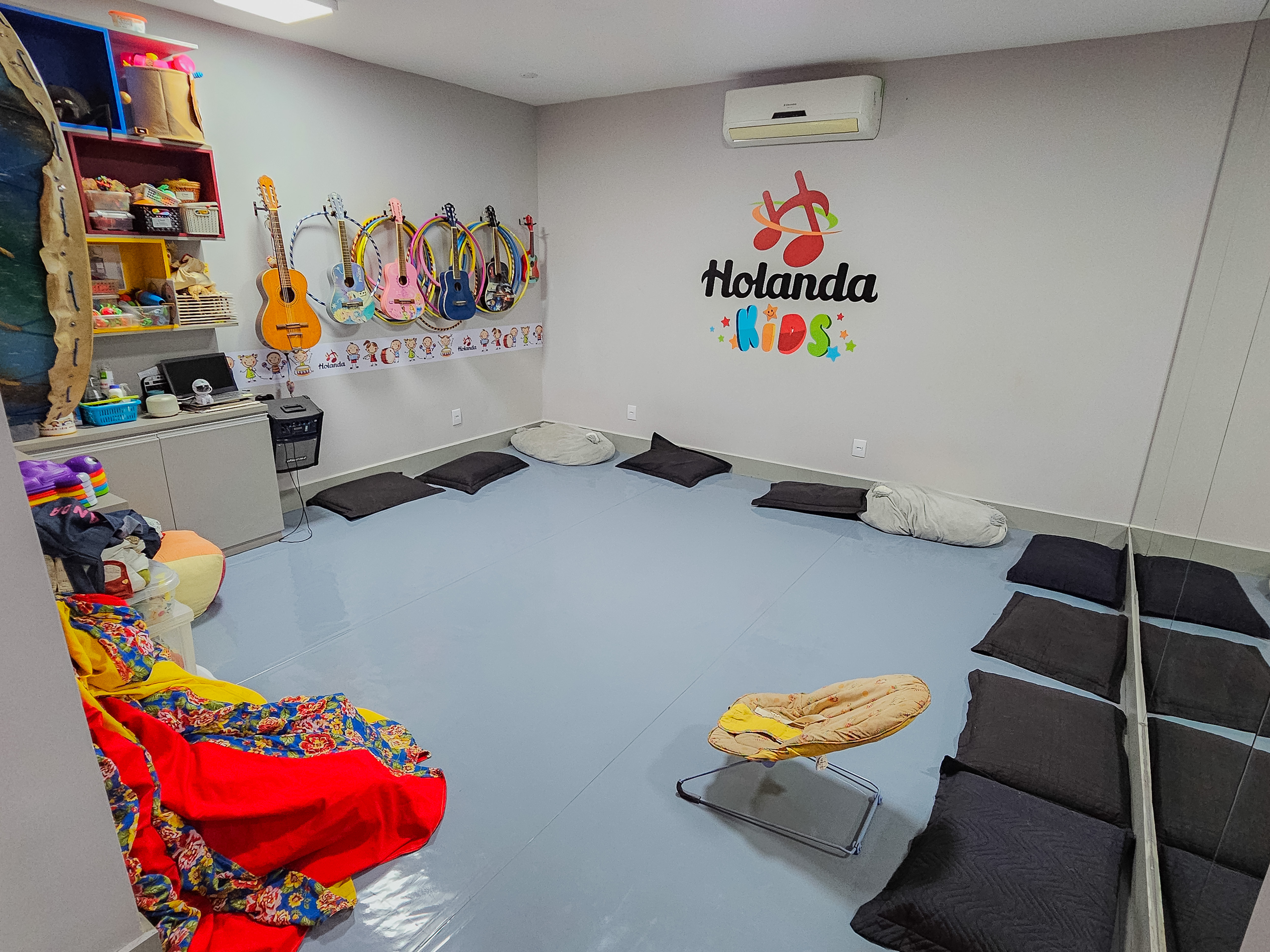 Sala Holanda Kids com violões coloridos, almofadas e logo