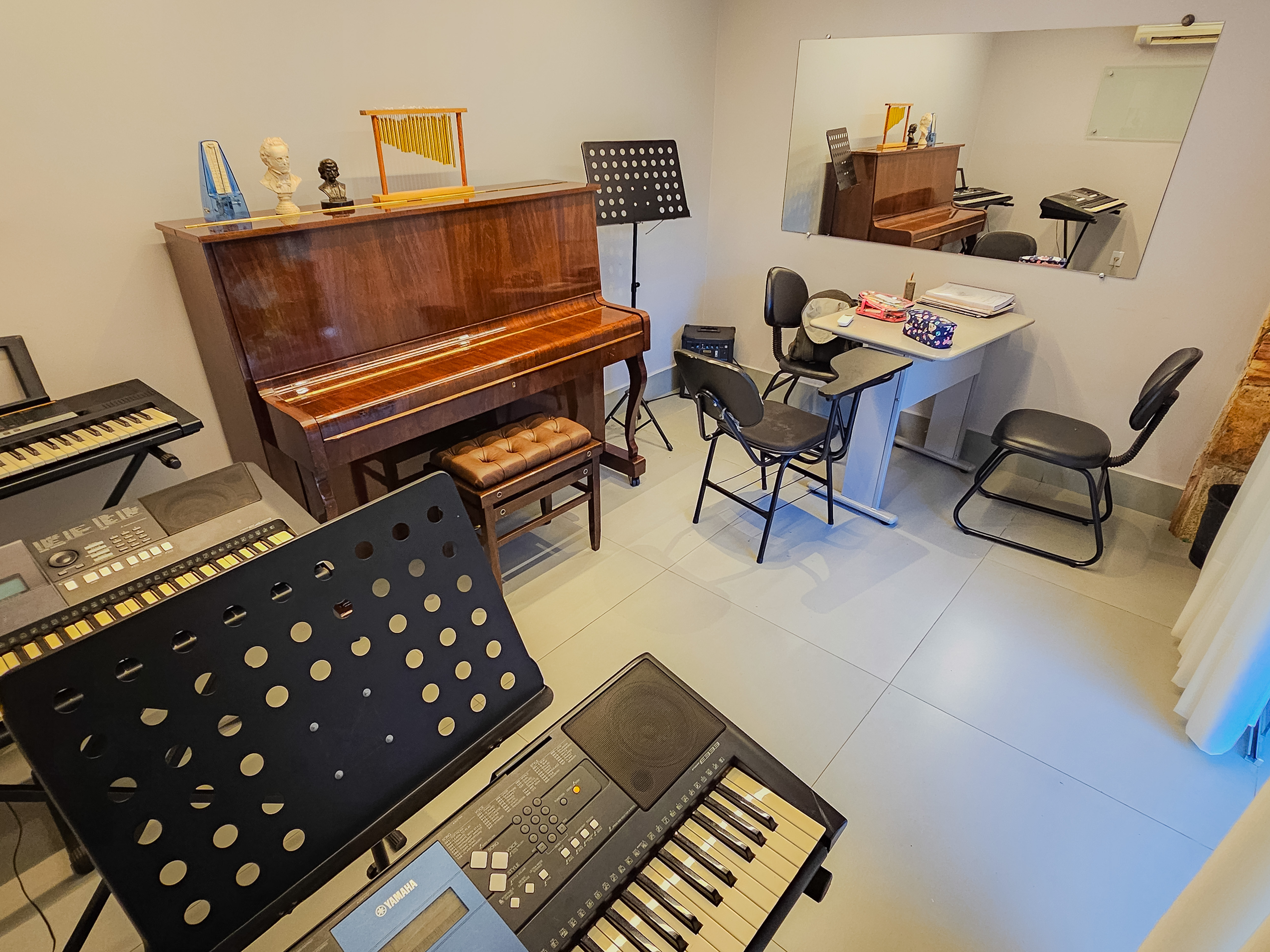 Sala de aula com piano, teclados e estantes de partitura